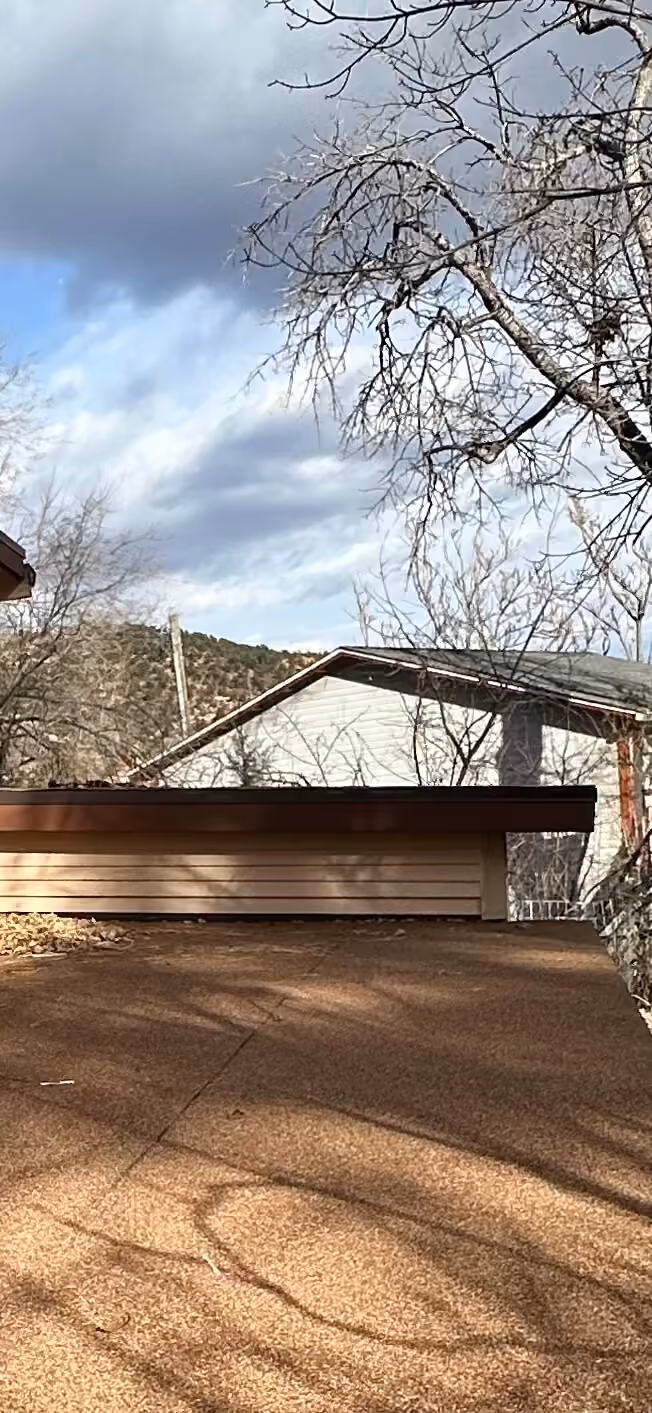 Finished low-slope roof surface and edge beneath trees and mountain sky