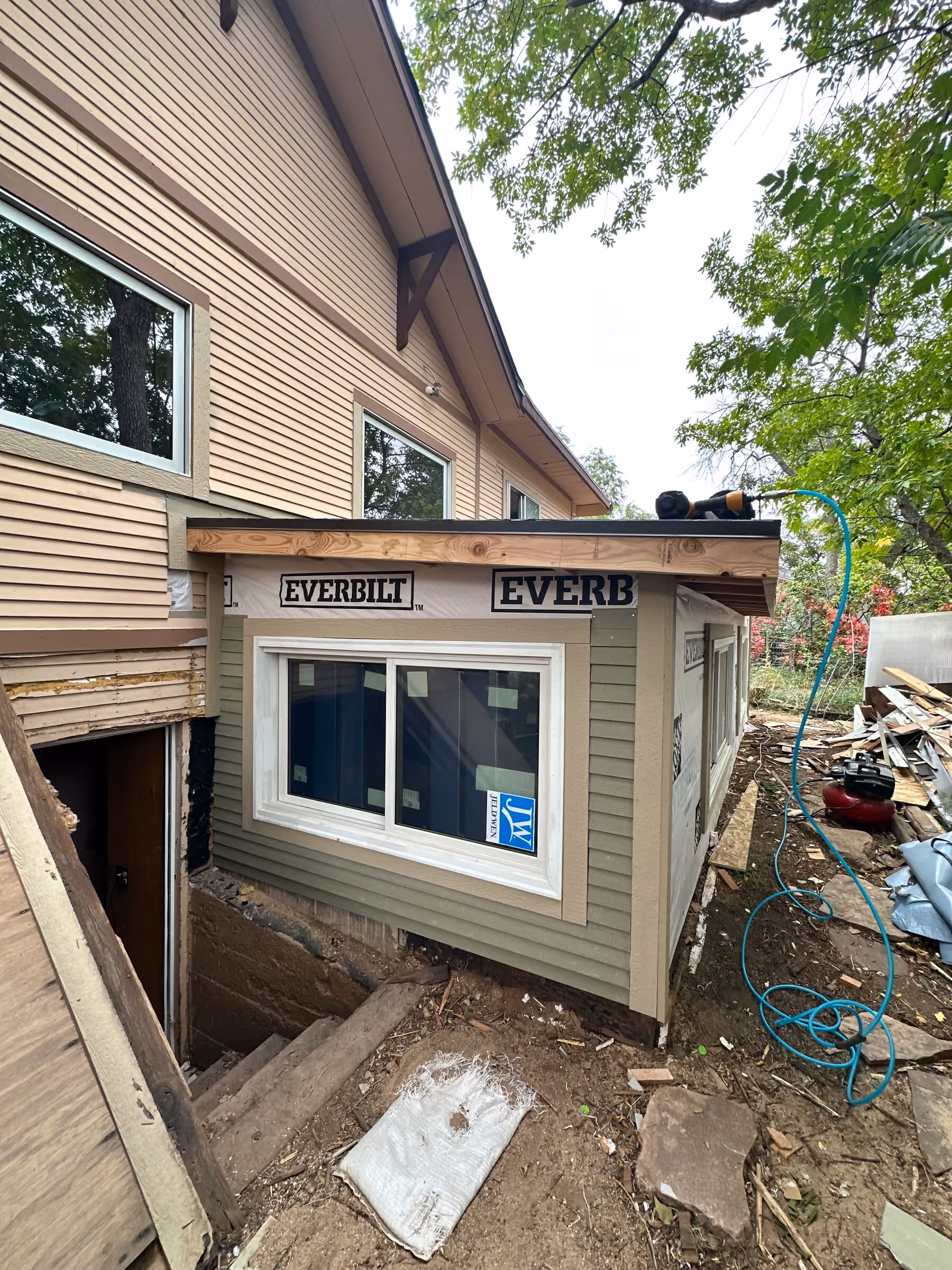 New exterior wall with an installed window, partial siding, and low-slope roof beside the house