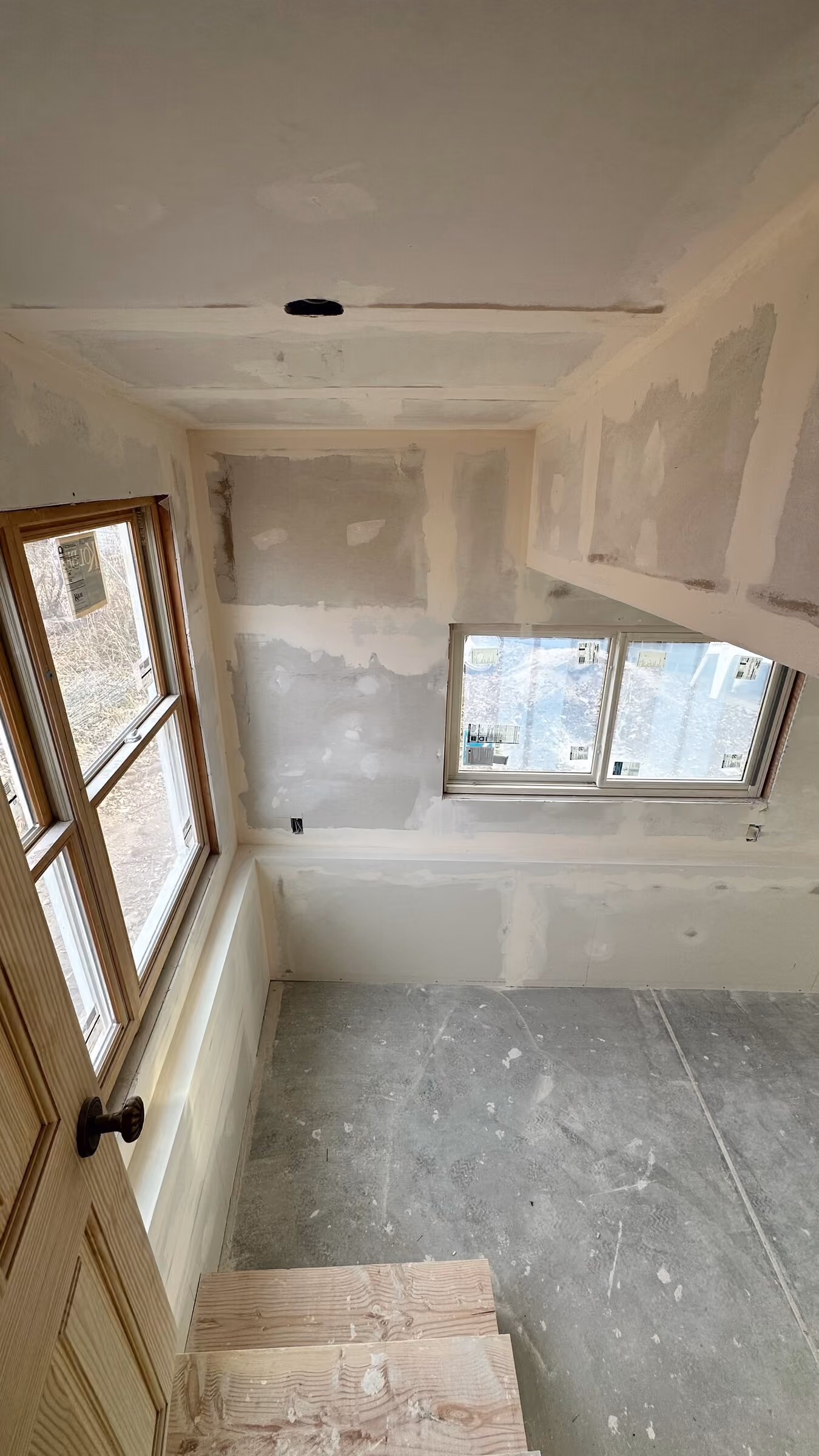 Unfinished addition interior with taped drywall, a door, and windows
